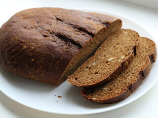 a loaf of rustic rye bread with two cut pieces on a white plate with a visible cut texture interspersed with grains and seeds, a healthy diet flour product on a white dish on a light surface