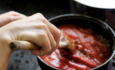 Cooking ground beef with tomato salsa. Focus on the cook's hand.