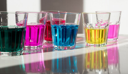 Colorful drink with dye in the glasses as a fun and experiment of child in kindergarten. Colored water and reflection of colors. Creativity and play. Closeup.