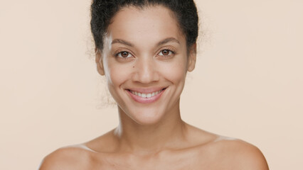 Close-up beauty portrait of young positive good-looking African American woman who smiles wide for the camera on beige background | Beauty and skin care commercial concept