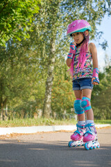 The girl is learning to rollerblade and is afraid to make the first movements, stands with a thoughtful look, doubt and fear. Kid  in a sports helmet, roller skates and protective equipment
