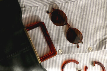 Striped shirt, leather bag, brown sunglasses and tortoiseshell pattern sunglasses. Flat lay.