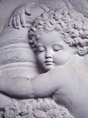 An old, weathered sandstone relief which shows a young, overweight angel who holds an urn.