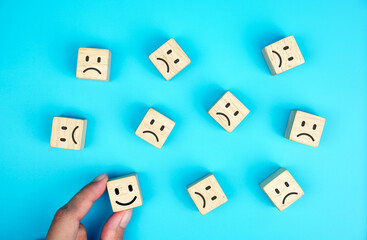 female hand chooses the happy face among unhappy faces on wooden blocks. Concept of customer satisfaction or positive feedback.                         