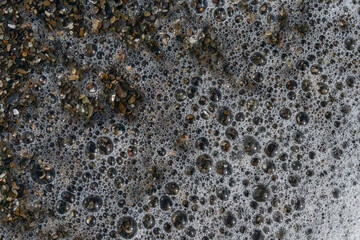 top view of a foamy sea wave breaking on a summer pebble beach