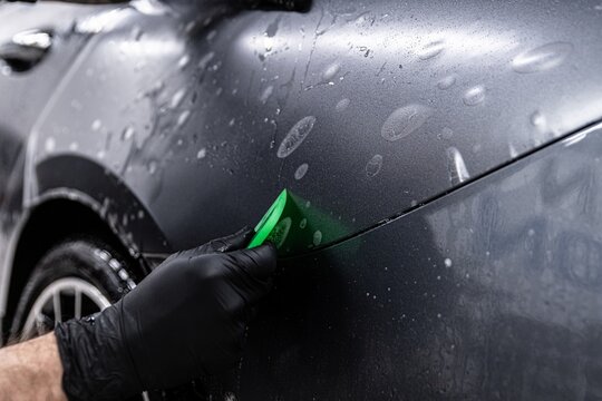 Car detailing studio worker applying transparent foil on car body