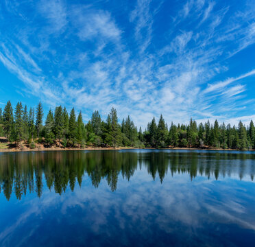 Panoramic scenic view of Lake Tabeaud surrounded by pine and cedar trees under beautiful blue sky
