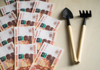 Russian paper money. Rubles next to garden tools. Shovel and rake. 5000 ruble banknote. Finance....
