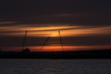 Naklejka na ściany i meble SUNRISE IN COAST - Cranes at the construction site in the sea port 