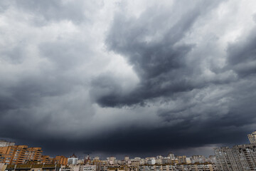 Dramatic stormy sky with the symbol of a flying bird or angel with wings, created of clouds over modern city district.