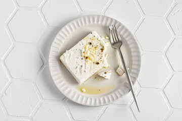 Eating Feta cheese on plate with olive oil with pepper. Tile background, top view