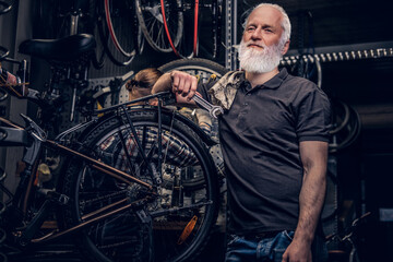 Obraz na płótnie Canvas Aged man mechanic repairing bicycles indoors his workshop
