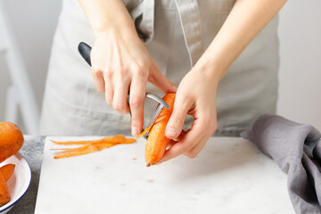 Hands cut carrot on marble board. Woman in apron cut carrot with peeler. Food preparing. Peel carrot, Vegetable