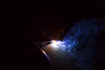 Arc welding. Welding of two sheets of metal by electrode in inert gases. Type MMA. A bright flash of light and a sheaf of sparks in a cloud of smoke. Miniature Universe. Free space for inscriptions.