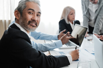 Business senior Asian man smiling at camera while working inside bank office - Focus on face