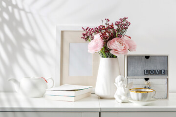 Bouquet of pink Persian buttercups on a white table in front of a chest of drawers. Scandinavian style. Place for text