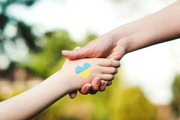 Ukrainian child holds a volunteer's hand. The kid painted the colors of the Ukrainian flag by hand.
