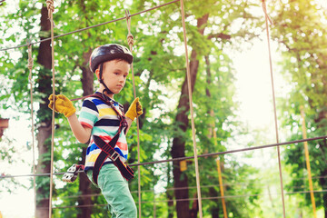 Young boy passing the cable route high among trees. Boy wearing helmet and safety equipment.