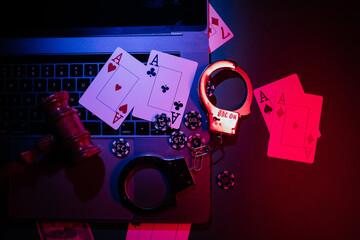 Prohibited gambling concept with cards, handcuffs, wooden gavel and chips on a laptop