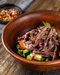 Deep plate with hot vegetables and beef. On a wooden table is a mug of light beer, spices and tomatoes. Menu for bar, cafe, restaurant. Dish from the chef. Close up