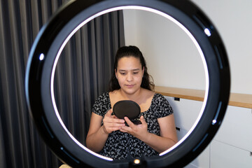 joven mujer se mira al espejo frente a aro de luz en interior de su recámara