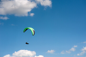 Alone green paraglider flying in the blue sky against the background of clouds. Paragliding in the...
