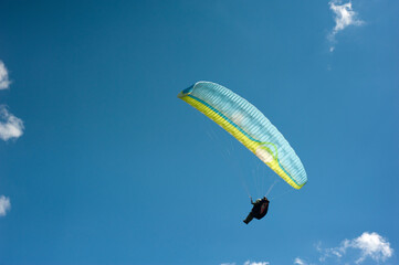 Alone blue and yellow paraglider flying in the blue sky against the background of clouds....
