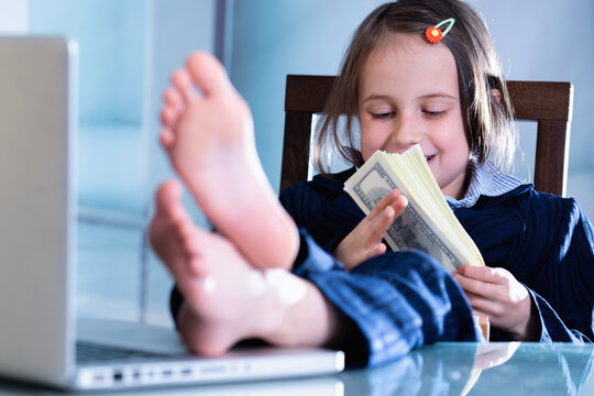 Conceptual image: making money and good business. Beautiful young girl put her feet up on a table and plays with US Dollar money. Horizontal image.
