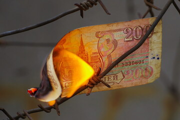 Burning russian banknote against the background of barbed wire. Сoncept Russian economy collapse 2022