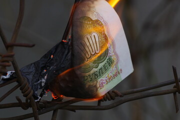 Burning russian banknote against the background of barbed wire. Сoncept Russian economy collapse...
