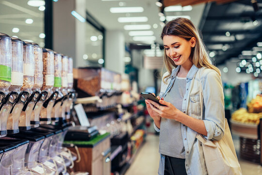 Woman using mobile phone and choosing product in supermarket
