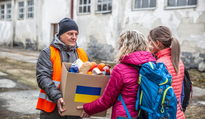 Volunteer in orange west gives a box of food donation to fleeing refugees from Ukraine - obrazy, fototapety, plakaty