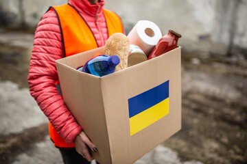 NGO volunteer carries a box with basic food and toilet papier with a Ukrianian flag sticker on the cardboard