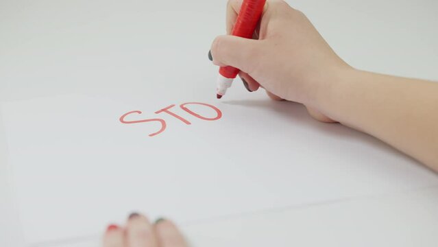 Caucasian female hand writing Stop sexism on white paper with red marker. Close-up unrecognizable activist drawing attention to social problems