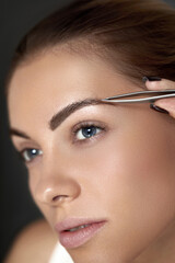 Eyebrow correction.  Plucking eyebrows. Beautiful young woman with tweezers. Model with beauty Face.  Natural Makeup