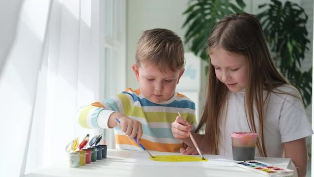 Brother and sister draw a picture with paints on a piece of paper. Children are learning to draw. Home creativity.