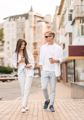 guy with a girl in white clothes walks around the city and drinks coffee