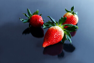 Time for healthy vitamin berries: three strawberries close-up on a shiny table surface, shadows from objects, space for text