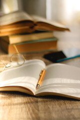 Open book, mechanical pencil, reading glasses, mobile phone and strack of books on the desk. Studying concept. Selective focus. 