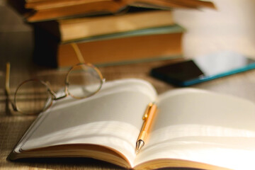 Open book, mechanical pencil, reading glasses, mobile phone and strack of books on the desk. Studying concept. Selective focus. 