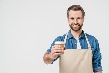 Confident caucasian young man bartender barista in apron selling giving coffee paper cup hot beverage for takeaway food isolated in white background