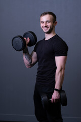 Fototapeta na wymiar A guy with dumbbells in a black T-shirt muscular man sport posing, from aged grey in guy and workout athletic, attractive caucasian. Active bodybuilder exercise, gym young