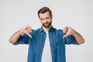 Negative opinion concept. Caucasian young man in denim casual clothes showing thumb down for...