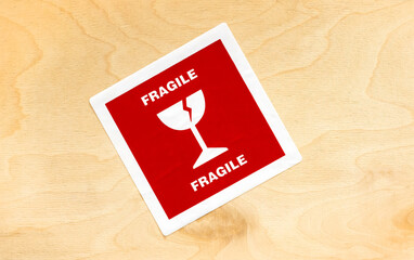 Red fragile cargo package sticker label on a wooden box crate container, detail, closeup, top view, from above, nobody. Cracked wine glass symbol. Logistics, fragility, delivery transportation concept