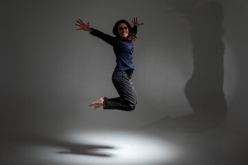 Fototapeta na wymiar Portrait of a cheerful positive girl jumping in the air with raised fists, looking at the camera, isolated on a light background, low key. Energy concept of people's lives. Place for inscription