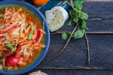 Spicy papaya salad served in a blue dish with sticky rice in a bucket and long beans, dried chilli and vegetables.