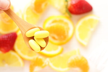 Vitamins pills on wooden spoon with lemon, orange, raspberry on background