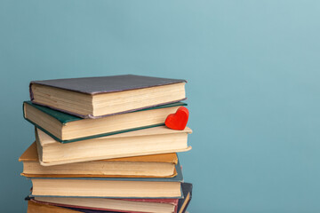 Stack of old books and little red heart on blue background. World Book Day poster. Copy space for text