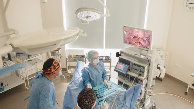 Surgeons team looks at monitors while preforming operation in hospital operating theater, male surgeon operating patient working with surgical laparoscopy instruments. Gynecology. Close up.