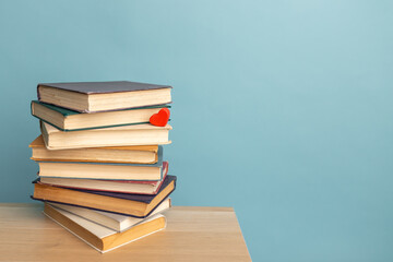 Stack of old books and little red heart on the table. World Book Day poster. Copy space for text